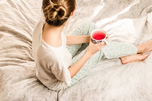 woman sitting on bed drinking tea facing away from camera