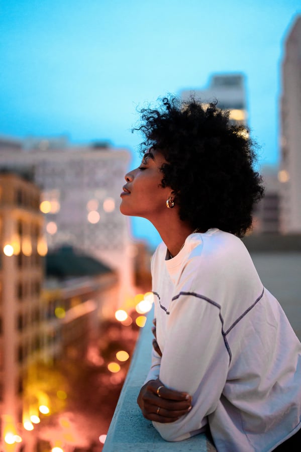 woman standing on balcony with eyes closed in contemplation